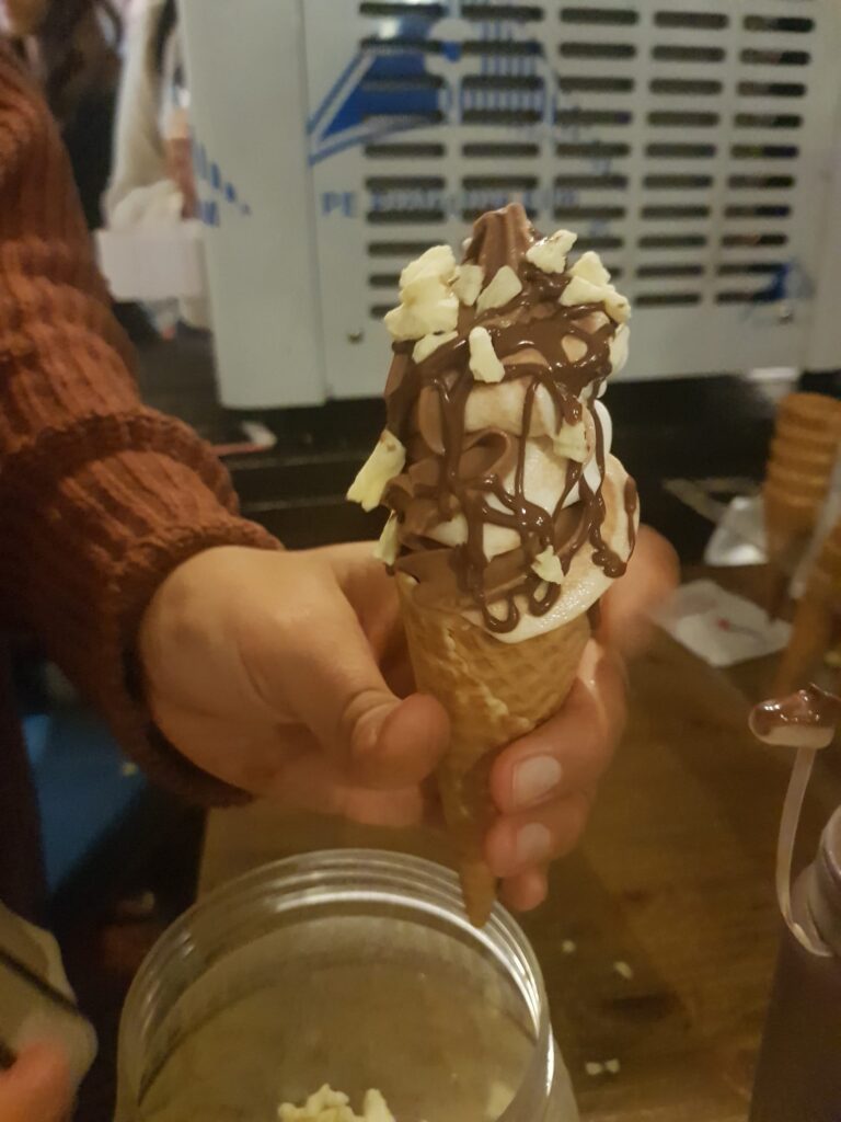 יד אוחזת בגביע גלידה עם זיגוג שוקולד ושבבי שוקולד לבן.