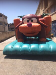 טירת קפיצות מתנפחת בצורת כלב מצויר מוצבת בחוץ בין שני בניינים ביום שטוף שמש.