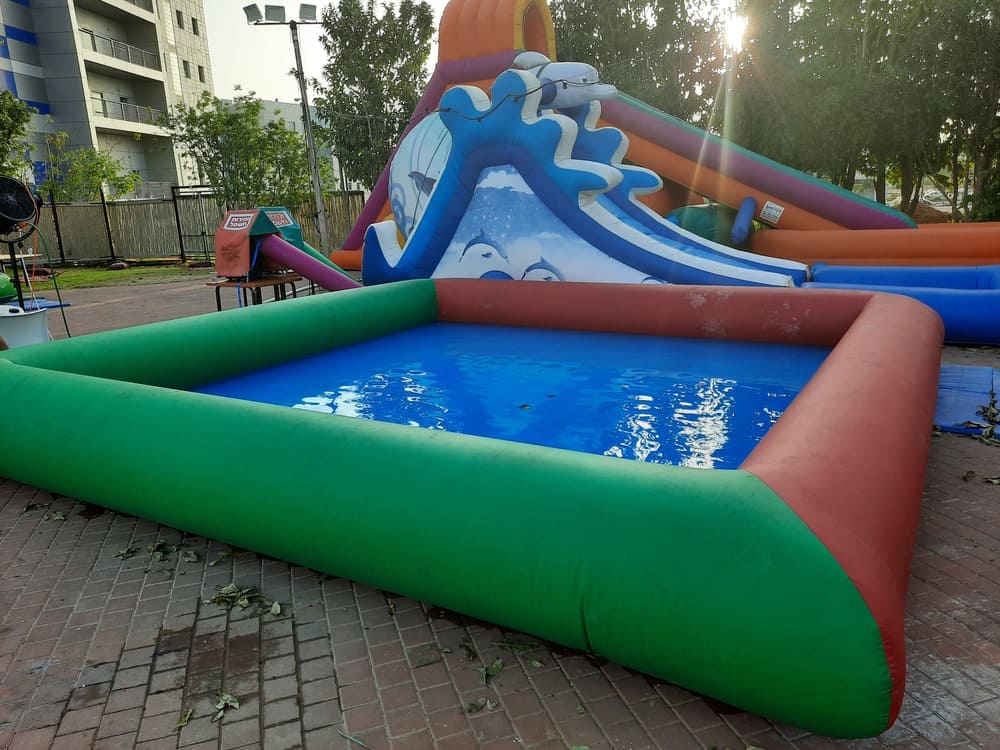 בריכה מתנפחת קטנה עם מים צלולים, לצד מגלשה מתנפחת צבעונית על משטח לבנים בחוץ.