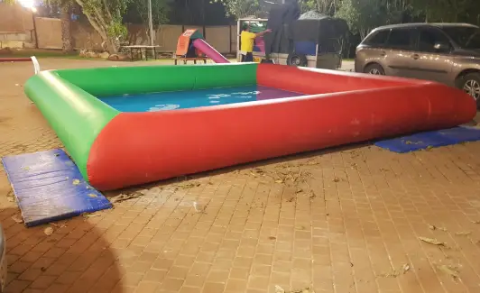 בריכה מתנפחת מלבנית, שדפנותיה אדומות וירוקות, מוצבת בלילה בשטח מרוצף בחוץ.